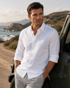 Man in a white shirt leaning against a vehicle with a scenic background